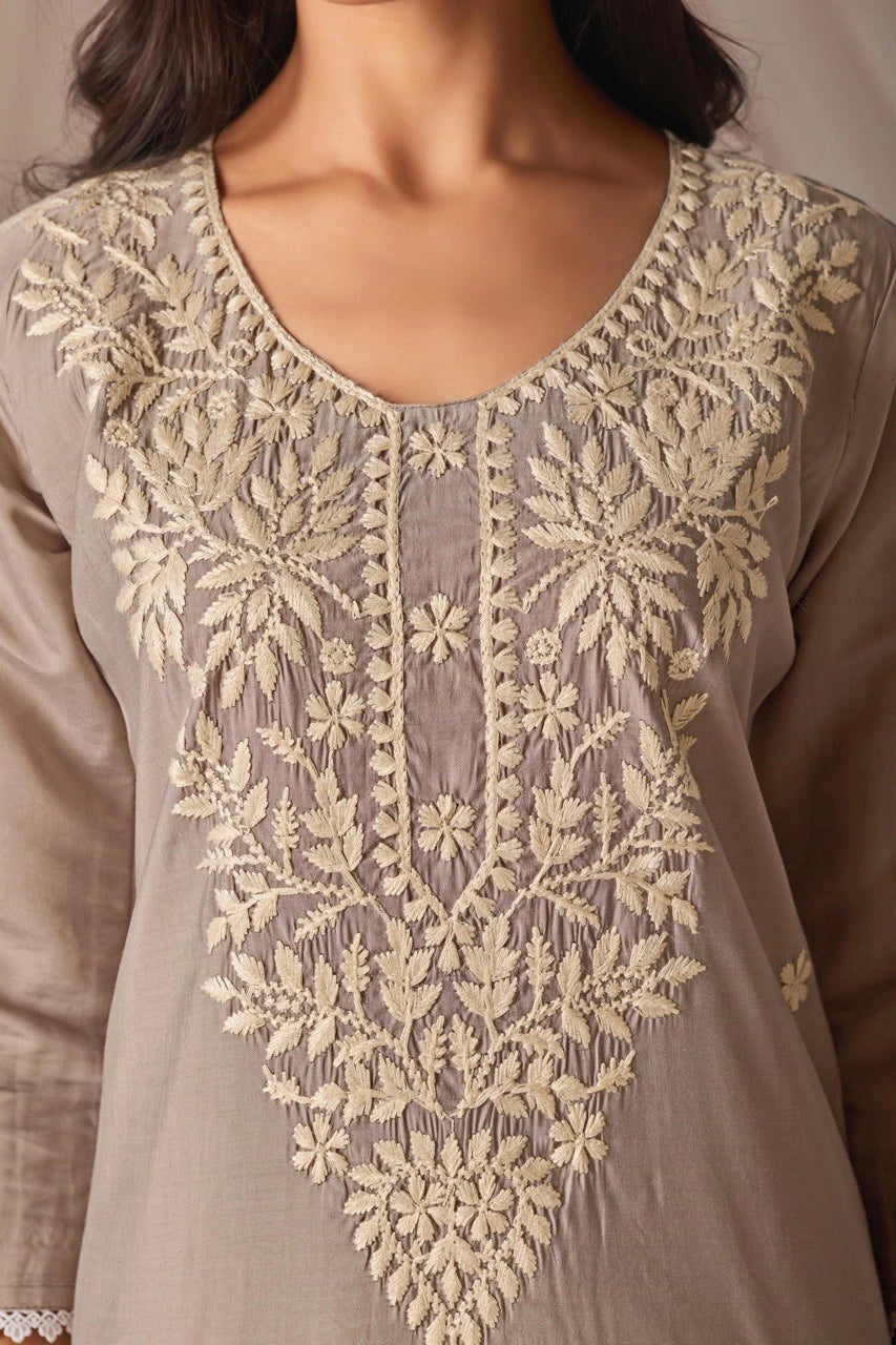 Close-up of a gray shirt with intricate beige embroidery on a neutral background